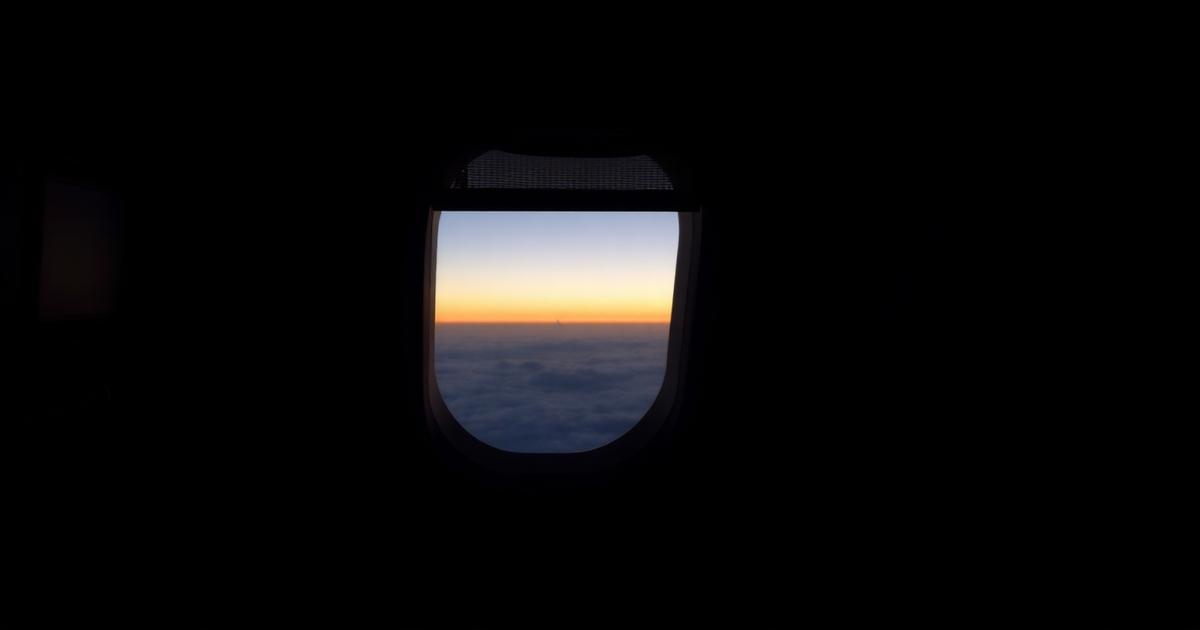 A darkened aircraft cabin with one window shade open onto a dawn horizon